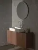 Waschtisch mit einer weißen Senke auf Holzunterbau und verchromter Armatur von Ideal Standard, ovaler Spiegel über dem Waschbecken an grauer Wand.